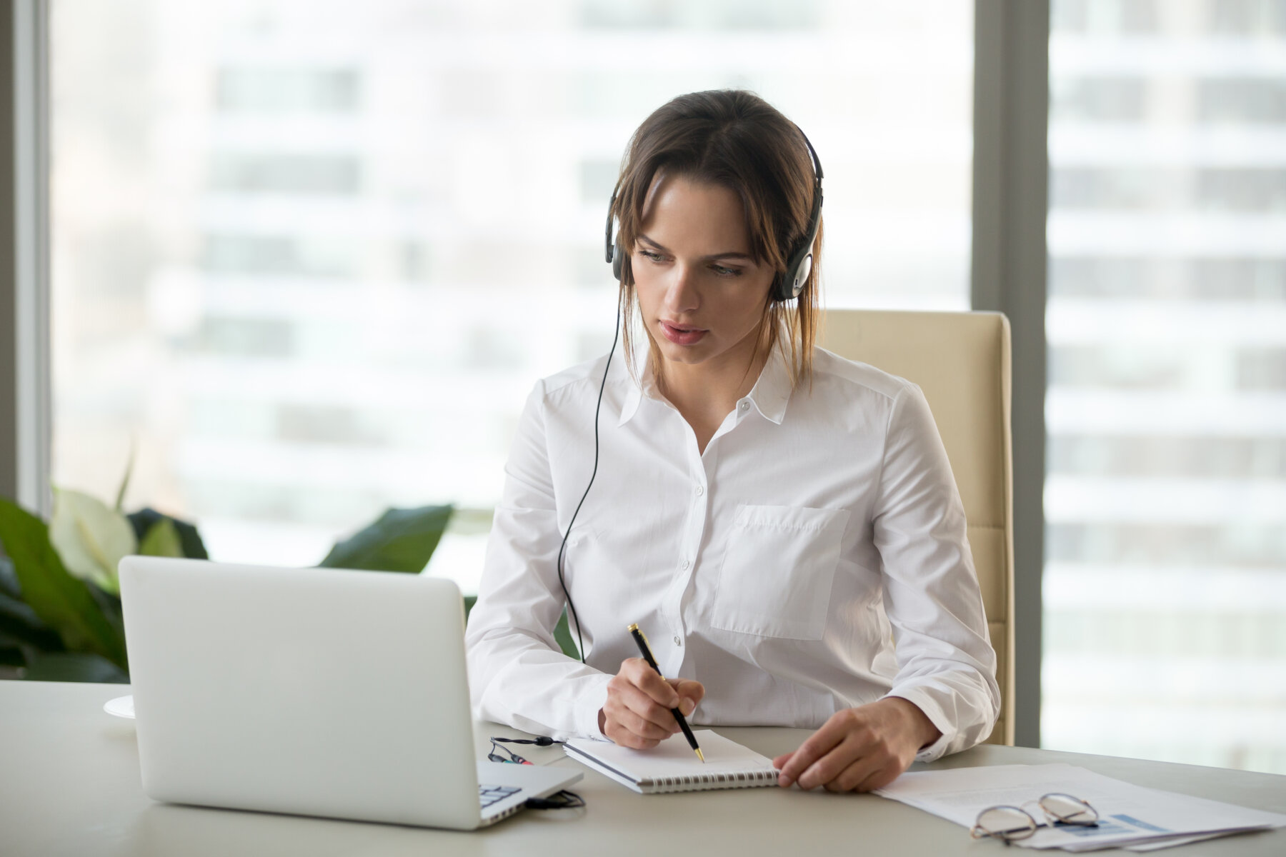 Serious,Businesswoman,In,Headphones,Watching,Webinar,On,Laptop,Making,Notes,