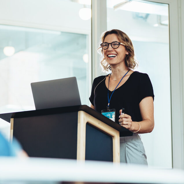 Businesswoman,Standing,At,Podium,With,Laptop,Giving,A,Speech.,Successful